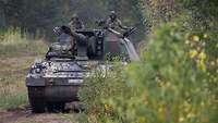 Eine Panzerhaubitze mit gesenktem Rohr auf der Marschfahrt im Gelände 