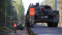 Mithilfe von zwei Soldaten als Einweiser wird ein Panzer auf einen Flachwagen der Deutschen Bahn gefahren.