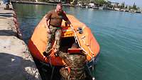 Eine Rettungsinsel schwimmt im Wasser, ein Soldat klettert hinein ein zweiter Soldat steht auf der Insel