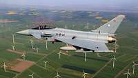 Ein Kampfflugzeug Eurofighter der Bundeswehr über einem Windpark.