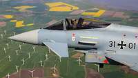 Ein Kampfflugzeug Eurofighter der Bundeswehr fliegt über einen Windpark.