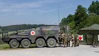 Ein Sanitätsfahrzeug vom Typ Boxer. Soldaten laden einen Patienten aus. Im Hintergrund eine Rettungsstation der Bundeswehr.