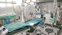 In der Mitte steht ein Operationstisch, um ihn herum mehre medizinische Geräte.