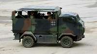 Ein Einsatzfahrzeug Spezialisierte Kräfte Mungo fährt mit sechs Soldaten über einen Platz.