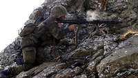 Ein Bundeswehrsoldat schießt kniend mit einem MG3 aus einer steinigen Berglandschaft heraus. 