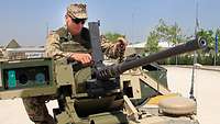 Ein Soldat sitzt hinter einem Maschinengewehr und entnimmt den Patronengurt mit der linken Hand.