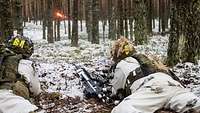 Zwei Soldaten tragen den weißen Schneetarnanzug und liegen im Wald, während sie eine Granatpistole abfeuern.