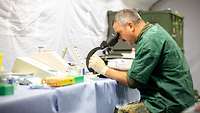 Ein Soldat in OP-Kleidung blickt durch ein Mikroskop