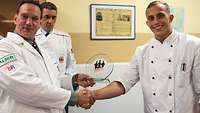 Männliche Person in Kochkleidung gratuliert weiterer mänlicher Person in Kochkleidung