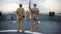 Drei Soldaten stehen vor der Bundesdienstflagge an Deck eines Schiffes.