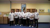 Gruppenbild mit acht männlichen Personen in Kochkleidung