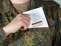 Soldat zieht Grundgesetzbuch aus der linken Brusttasche seiner Uniform.