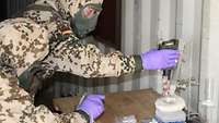 Soldaten in Schutzanzügen überprüfen eine Flüssigkeit auf chemische Kampfstoffe.