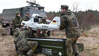 Drei Soldaten verpacken eine Aufklärungsdrohne in einem Waldstück in eine Kiste.