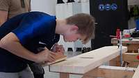Ein Jugendlicher bearbeitet in einer Werkstatt mit einem Hobel ein Holzstück.