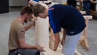 Ein Soldat hilft in einer Werkstatt einem Schüler bei der Montage eines Holzstuhls.