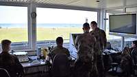 Vier Soldaten im Schießkontrollturm überwachen das scharfe Schießen bei der Übung Tobruq Legacy am Monitor.