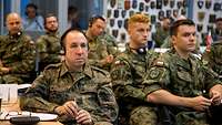 Mehrere Soldaten sitzen zu einem Redner gewandt und hören ihm zu.