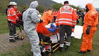 Sanitäter und Feuerwehrleute in signalfarbenen und silberglänzenden Schutzanzügen kümmern sich um einen Verletzten