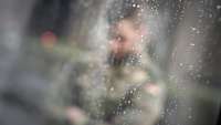 Ein Soldat im Flecktarnanzug ist verschwommen hienter einer Glasscheibe mit Regentropfen erkennbar