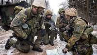 Soldaten knien auf dem Waldboden über einer Karte.