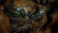Ein Soldat sitzt in einem unterirdischen Versteck und hat ein Tablet in der Hand.