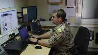 Ein Soldat sitzt am Schreibtisch vor dem Computerbildschirm
