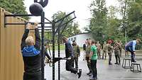 Zwei Soldaten treiben Sport an einem Fitness-Container. Im Hintergrund stehen mehrere Soldaten.