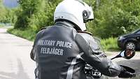 Motorradfahrer im grauen Lederkombi mit weißem Helm. Rückenaufschrift: „Military Police – Feldjäger“. 