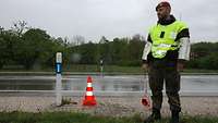 Feldjäger mit Warnweste, Armstulpen und Kelle steht im Regen an einer Straße, neben ihm ein orangefarbener Pylon.