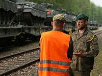 Zwei Soldaten im Gespräch, im Hintergrund mehrere Panzer verladen auf Eisenbahnwagen