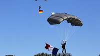 Zwei Fallschirmspringer segeln jeweils mit einer deutschen und einer französischen Flagge zu Boden.