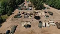 Luftbild mit vielen Zelten und Wassertanks in verschiedenen Formen. Im Hintergrund Wald. 