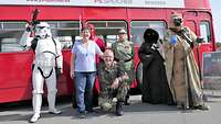 Sieben Menschen, darunter fünf in Kostümen aus dem Film „Star-Wars", vor einem Doppeldeckerbus