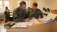 Zwei Soldaten stehen in einem Büro an einem Tresen und sichten gemeinsam Papiere.