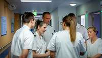 Medizinisches Personal steht im Flur eines Krankenhauses im Kreis und bespricht den weiteren Fortgang der Visite
