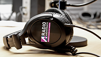 Kopfhörer mit dem Radio Andernach Logo im Fokus. Sie liegen auf dem Tisch in einem Tonstudio. 