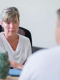 Ein PTBS Erkrankter sitzt einer Therapeutin im Gespräch an einem Tisch gegenüber