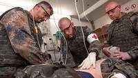 Drei Sanitäter versorgen einen auf einem Behandlungstisch liegenden Patienten