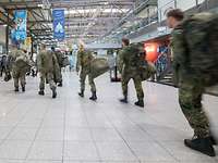 Mehrere Soldaten in Flecktarn Uniformmit Gepäck betreten die Halle eines Flughafens.