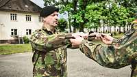 Ein Soldat in niederländischer Uniform erhält von einem Soldaten in deutscher Uniform den Cane, einen schwarzen Stock.