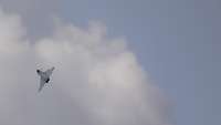 Ein Kampfflugzeug dreht am mäßig bewölkten Himmel eine Flugkurve nach links