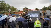 Eine Gruppe Menschen in Regenkleidung oder unter Regenschirmen auf einer Baustelle