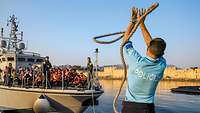 Ein Frontex-Mitarbeiter fängt das Seil eines im Hafen ankommenden Bootes mit Flüchtlingen an Bord