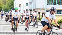 Radfahrer in einheitlichen Trikots starten eine Tour auf Asphalt vor einem Dienstgebäude
