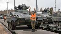 Ein Soldat steh auf einem Einsanbahnwaggon und zeigt dem Fahrer eines Panzers wie er steuern muss