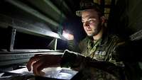 Ein Soldat sucht im Licht einer Taschenlampe in einem Regal ein kleines Ersatzteil.