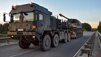 Ein Schwerlasttransporter fährt mit einer Panzerhaubitze beladen über eine Autobahnbrücke.