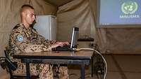 Ein Bundeswehrsoldat sitzt im Einsatz am Tisch und arbeitet an einem Laptop
