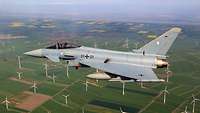 Kampfflugzeug Eurofighter fliegt über einen Windpark